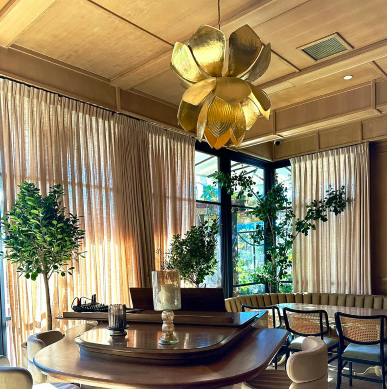 Warm dining lounge with curated trees and a gold lotus chandelier